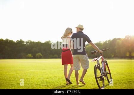Couple pushing cycle whilst strolling in park