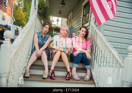 Portrait of young female friends sitting on porch steps Stock Photo