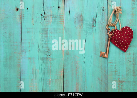 Bronze skeleton key and red heart hanging from rope on antique green distressed wood door Stock Photo