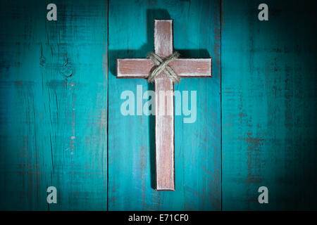 Spotlight on rugged wooden cross hanging on antique teal blue rustic wood background Stock Photo