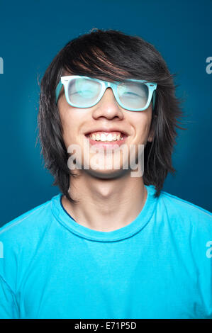 Close up portrait of a smiling happy hipster young Asian man wearing glasses. Blue colors Stock Photo