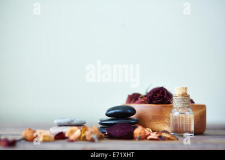 Dry roses in bowl, spa stones and aromatic essence in bottle Stock Photo