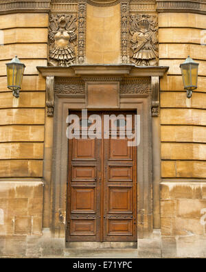 Ornate brown wooden double doors with rectangular panels and highly decorative carved stone frame in wall of historic building in Oxford, England Stock Photo