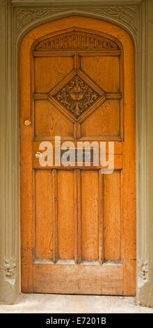 Golden brown wooden door with arched top and intricately carved designs on door and lighter brown frame in Oxford England Stock Photo