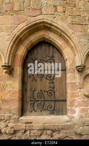 Arched wooden door with huge spectacular and decorative hinges in weathered stone wall at ruins of historic Bolton priory England