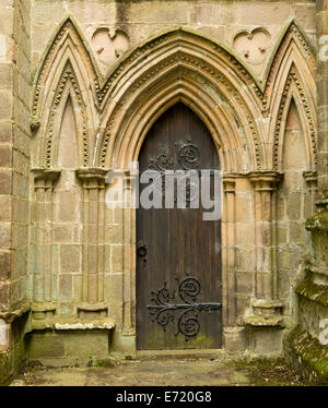 Wooden door with large & spectacularly decorative hinges surrounded by ornate stone arches at historic Bolton priory church in England Stock Photo
