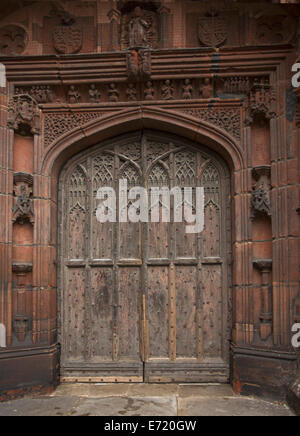 Spectacular arched wooden door with intricate carving surrounded by intricately carved red stonework at entrance to historic Chester cathedral England Stock Photo