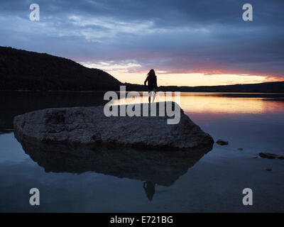 Lac de Chalain sunset, Jura, France with silhouetted person standing on a big rock. Stock Photo