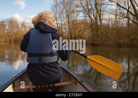 A woman in her 30's paddling in a canoe along a river on the Norfolk Broad Stock Photo