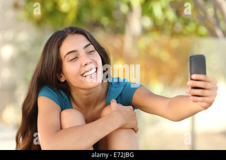 Happy laughing teen girl taking a selfie portrait with her smart phone in a park Stock Photo