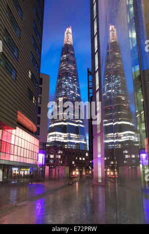The Shard reflecting in the windows of the modern office buildings of More London Place. Neon lights shine on the wet pavements. London, England, UK. Stock Photo