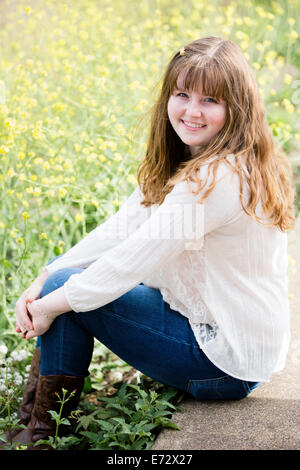 Portrait of teenage girl (13-15) sitting on wall in meadow Stock Photo
