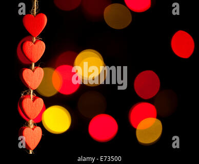 Red wooden hearts hanging on the rope. On a black background with bokeh. Stock Photo