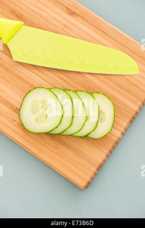 Cucumber slices and green knife on wooden cutting board Stock Photo
