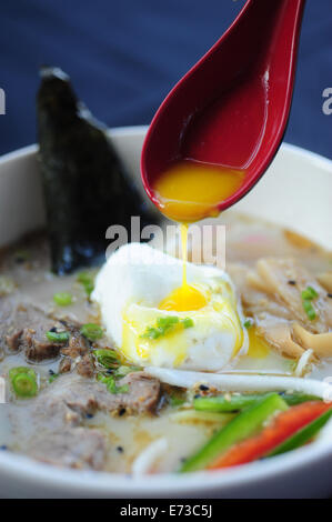 Food Dining Asian Japanese ramen noodle soup with an poached egg hand holding red spoon Stock Photo