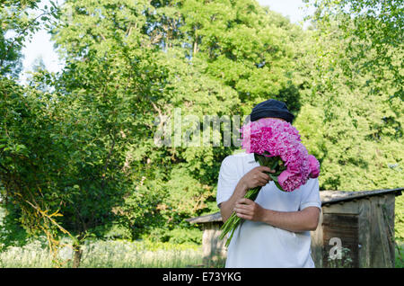 man hiding his face with large pink peony bouquet of spring garden Stock Photo