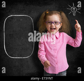 Happy kid girl in glasses with bright idea standing near school blackboard in classroom Stock Photo