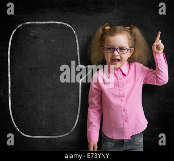 Funny child in eyeglasses standing near school chalkboard  as a teacher with blank speech bubble scetch. Stock Photo