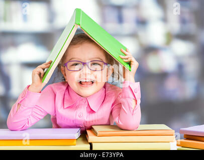 Little girl in glasses under roof made from book. Stock Photo