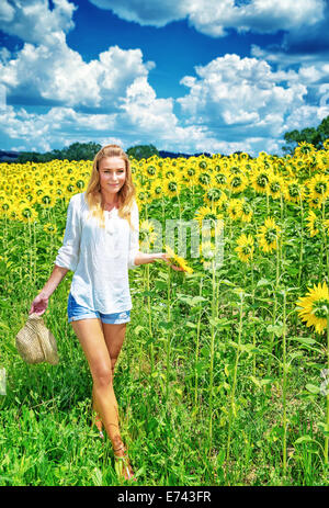 Beautiful young woman walking on fresh sunflowers field, majestic beauty of countryside nature, summer traveling concept Stock Photo