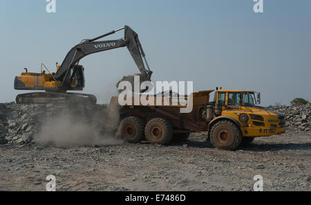 A Volvo mining dump truck is being loaded with rock by a Volvo excavator in a large African open cast copper mine. Stock Photo