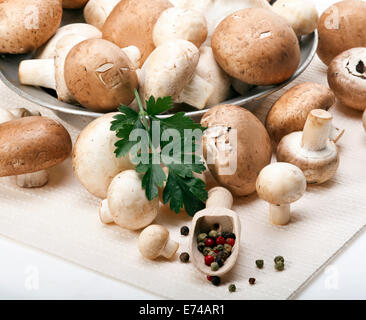 Button or Champignon and Portabello mushrooms in old metal plate with parsley and mixed pepper beans on a white tablecloth. Stock Photo