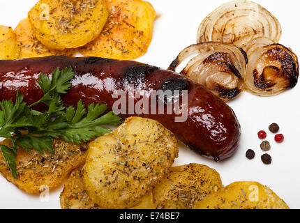 Baked sausage surrounded with black green and red pepperbeans slices of onion patatoes and parsley on a white plate. Stock Photo