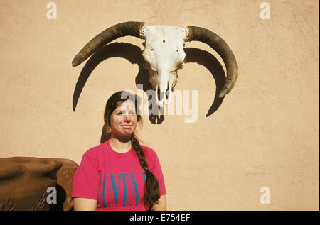 A woman leans against an adobe wall decorated with a bleached cow skull in downtown Santa Fe, New Mexico, near the Santa Fe Plaz Stock Photo