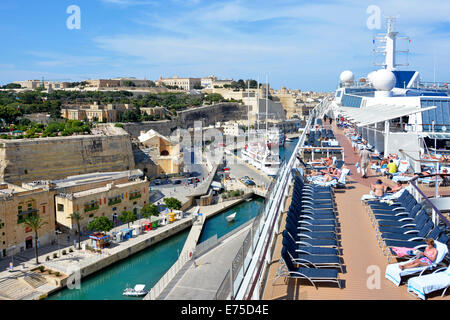 Sun deck of large tall modern ocean cruise ship liner & views of Valletta city & passengers sunbathing Grand Harbour Malta Mediterranean Cruise Europe Stock Photo