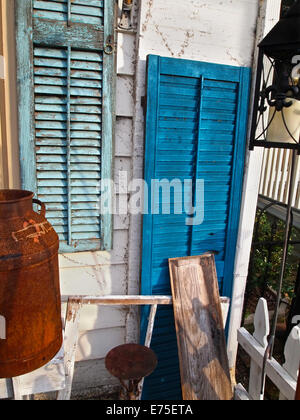 A display of old shutters with peeling paint on an aging porch full of vintage items. Stock Photo