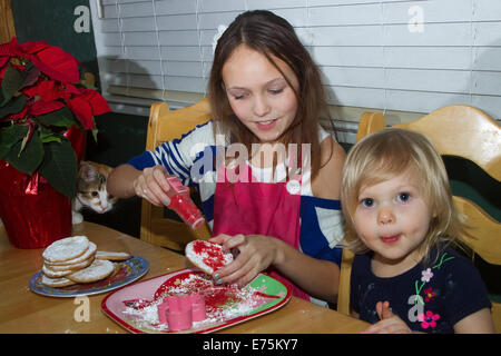 Sisters Decorating Cookies While Cat Looks On Stock Photo