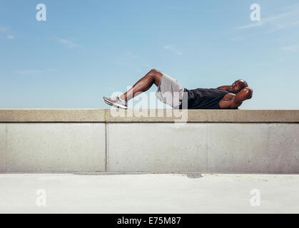 Muscular young man doing sit-ups looking at camera. African guy exercising outdoors with copy space. Stock Photo