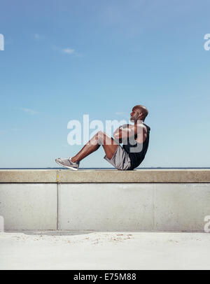 Side view of fit young man exercising outdoors. Muscular young man doing sit-ups against sky.