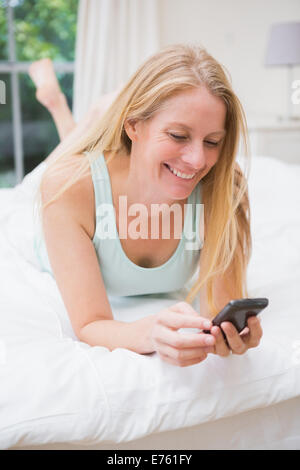 Happy blonde using smartphone on bed Stock Photo