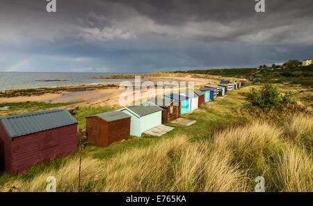 CHALETS AT HOPEMAN BEACH MORAY DARK CLOUDS AND A RAINBOW  OVER THE ROWS OF MULTI COLOURED HUTS Stock Photo