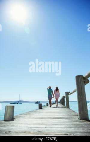 Couple holding hands walking along wooden dock