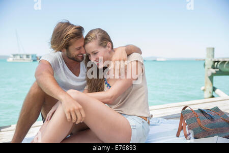 Couple sitting together on edge of wooden dock Stock Photo