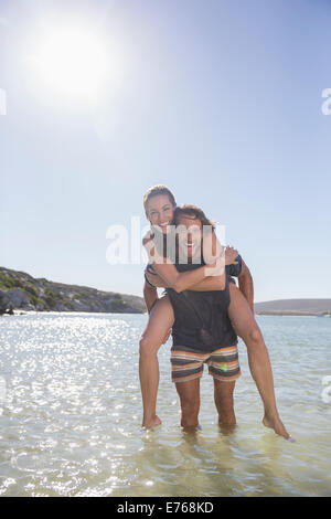 Woman being carried piggy back by boyfriend in waves Stock Photo