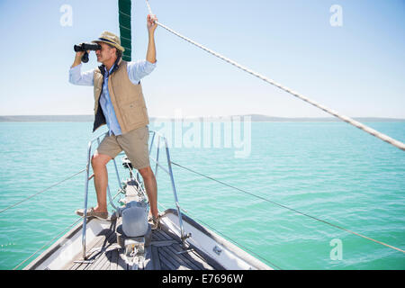 Older man looking out binoculars on edge of boat Stock Photo