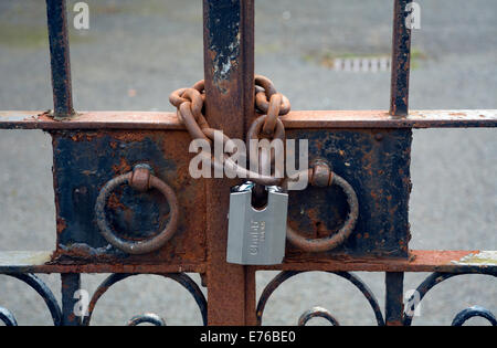 Ornate gates secured by a new padlock on a rusty chain. Stock Photo
