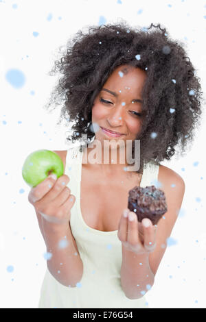 Composite image of young woman hardly hesitating between a muffin and an apple Stock Photo