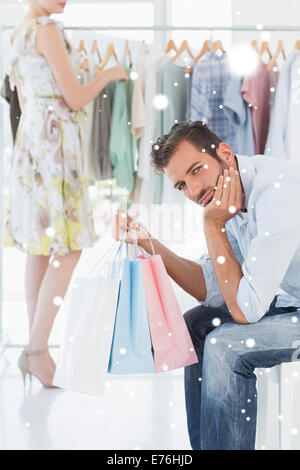 Composite image of bored man with shopping bags while woman by clothes rack Stock Photo