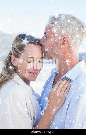 Composite image of man kissing his smiling partner on the forehead at the beach Stock Photo