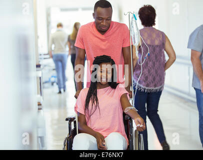 Man wheeling girlfriend in hospital hallway Stock Photo