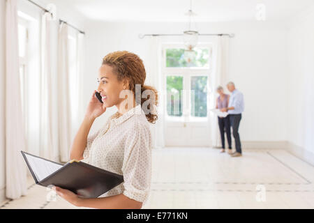 Woman talking on cell phone while couple looks at living room Stock Photo