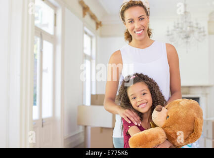 Mother and daughter smiling while clutching teddy bear Stock Photo