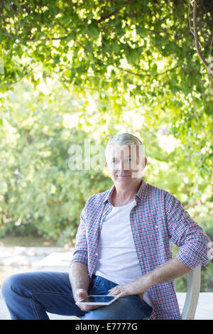 Older man sitting with digital tablet outdoors Stock Photo