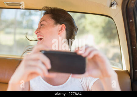Woman in car backseat taking picture with cell phone Stock Photo