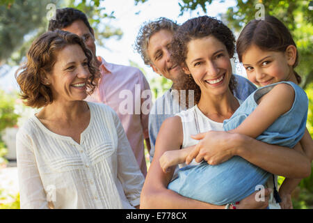 Mother carrying daughter in arms with family outdoors Stock Photo