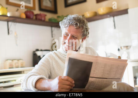 Older man reading news paper in kitchen Stock Photo